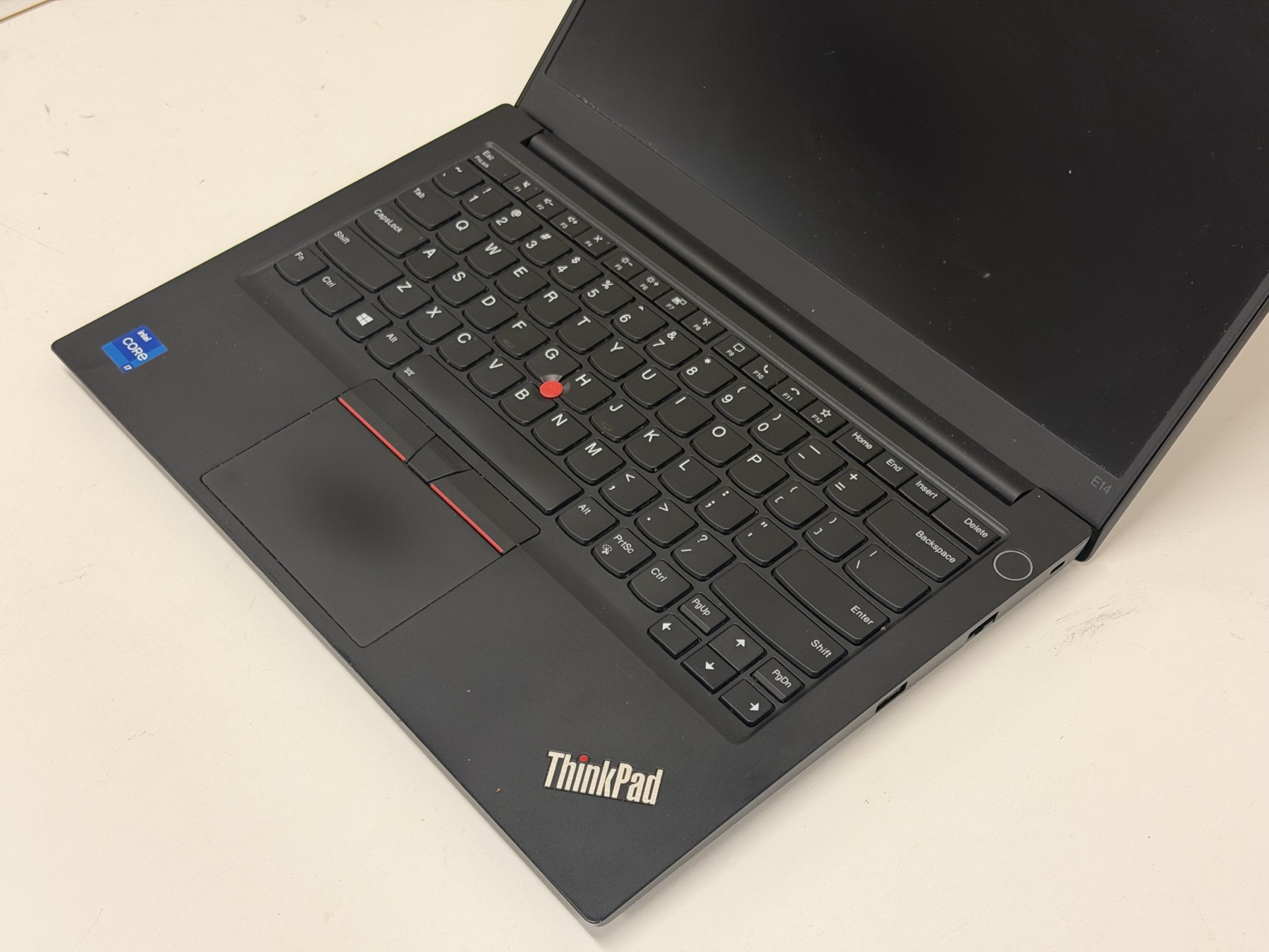 A ThinkPad E14 on the bench in our Perth workshop, lid open at an angle — the iconic red TrackPoint visible between the G, H and B keys, the red middle-click stripe on the UltraNav touchpad, and the ThinkPad wordmark on the palm-rest. Representing the keyboard, TrackPoint and palm-rest repairs we do daily.
